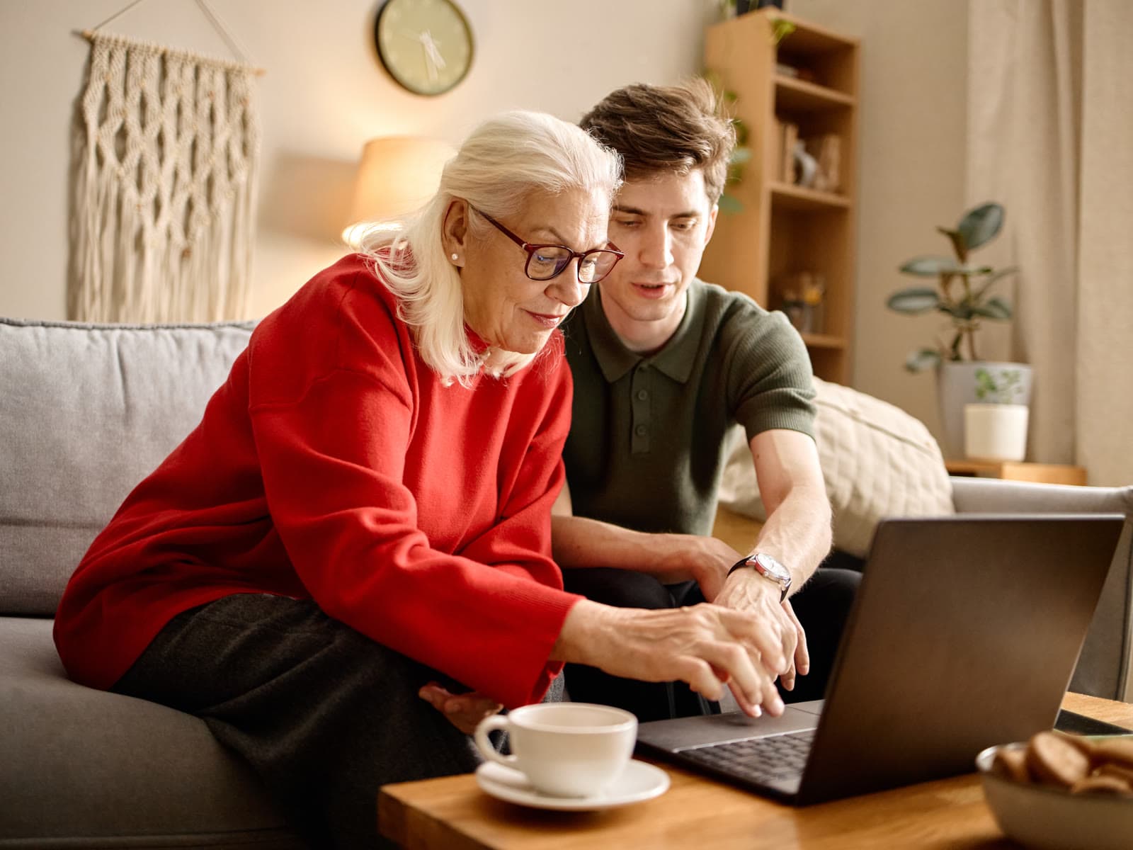 Two people sitting together on a sofa at home, looking at a laptop on the coffee table.
